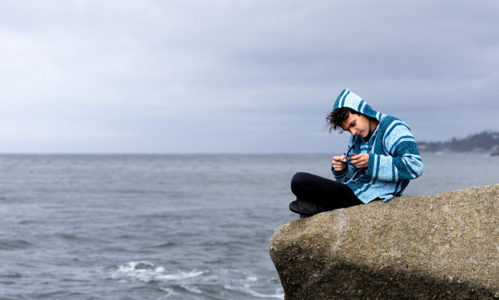 Teen in Baja hoodie sitting on rock